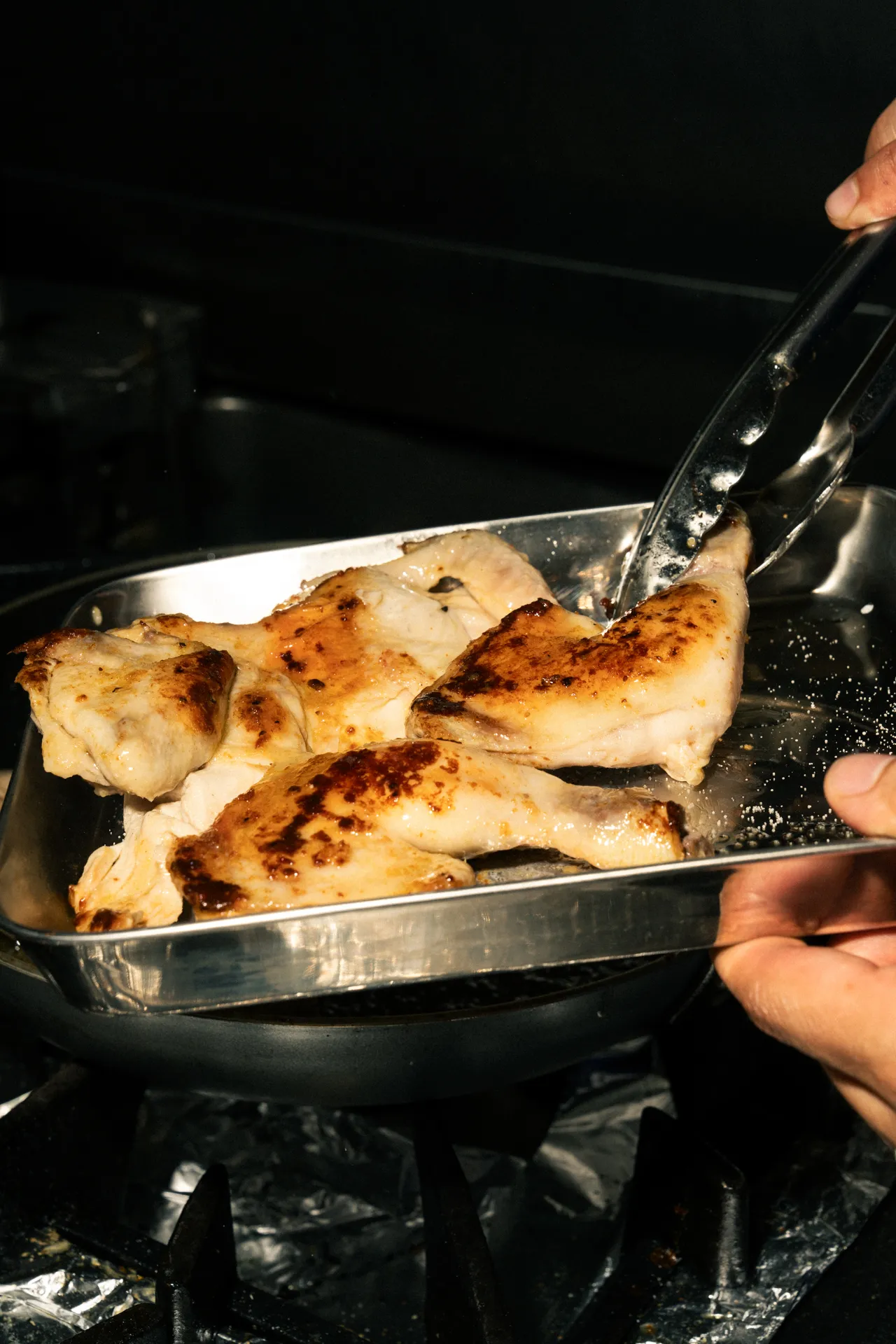 Poulet doré retourné à la pince dans un plat en inox