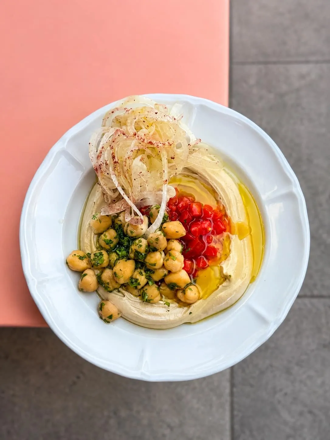 Tahini crémeux, pois chiches au citron et oignons émincés sur une assiette blanche
